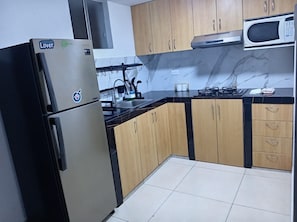 Een keuken met een roestvrijstalen koelkast, houten kastjes, een magnetron en een gasfornuis.
