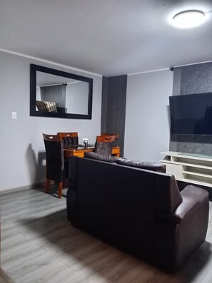 A living room with a sofa, a dining table with chairs, a TV, and a mirror on the wall.