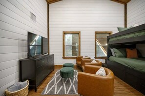 A cozy room with a bunk bed, a television, a dresser, and a seating area with a patterned rug. - Hot Tub + Game Room + Playground | Sleeps 14 (Broken Bow)