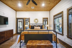 A bedroom with a bed, bedside tables, a TV, and a ceiling fan. - Hot Tub + Game Room + Playground | Sleeps 14 (Broken Bow)