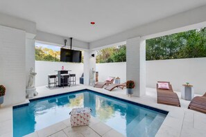 A modern outdoor pool area with a flat roof, a seating area with a table and chairs, and a television mounted on the wall. - Beach Access • Golf Cart • Sauna+ColdPlunge • Pool (Santa Rosa Beach)