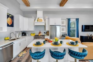 A modern kitchen with white cabinets, a central island with bar stools, and a dining area with a blue upholstered chair. - Beach Access • Golf Cart • Sauna+ColdPlunge • Pool (Santa Rosa Beach)
