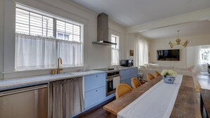 A modern kitchen with a central island, a dining area with a wooden table, and a living room with a sofa and TV. - Summery Southern Home in the Heart of Starland (Savannah)