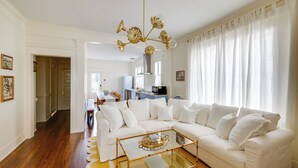A living room with a white sofa, a glass coffee table, and a chandelier. - Summery Southern Home in the Heart of Starland (Savannah)
