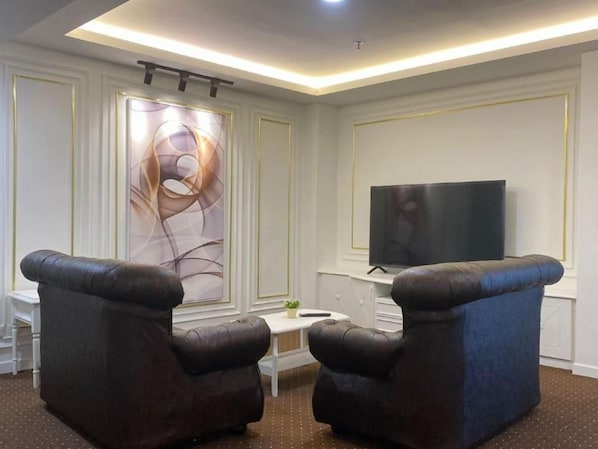 A living room with a flat-screen TV, two leather armchairs, a small white table, and a decorative wall piece.