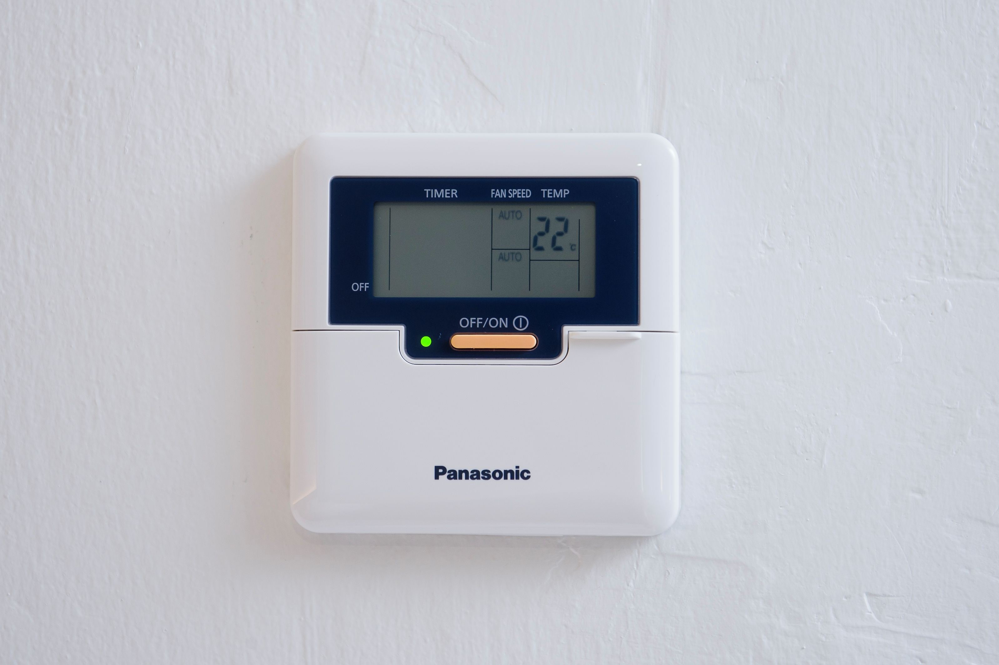 A Panasonic digital thermostat mounted on a white wall.