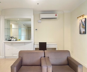 A living room with a sofa, a coffee table, a dining table with chairs, a kitchen area with cabinets, and an air conditioning unit.