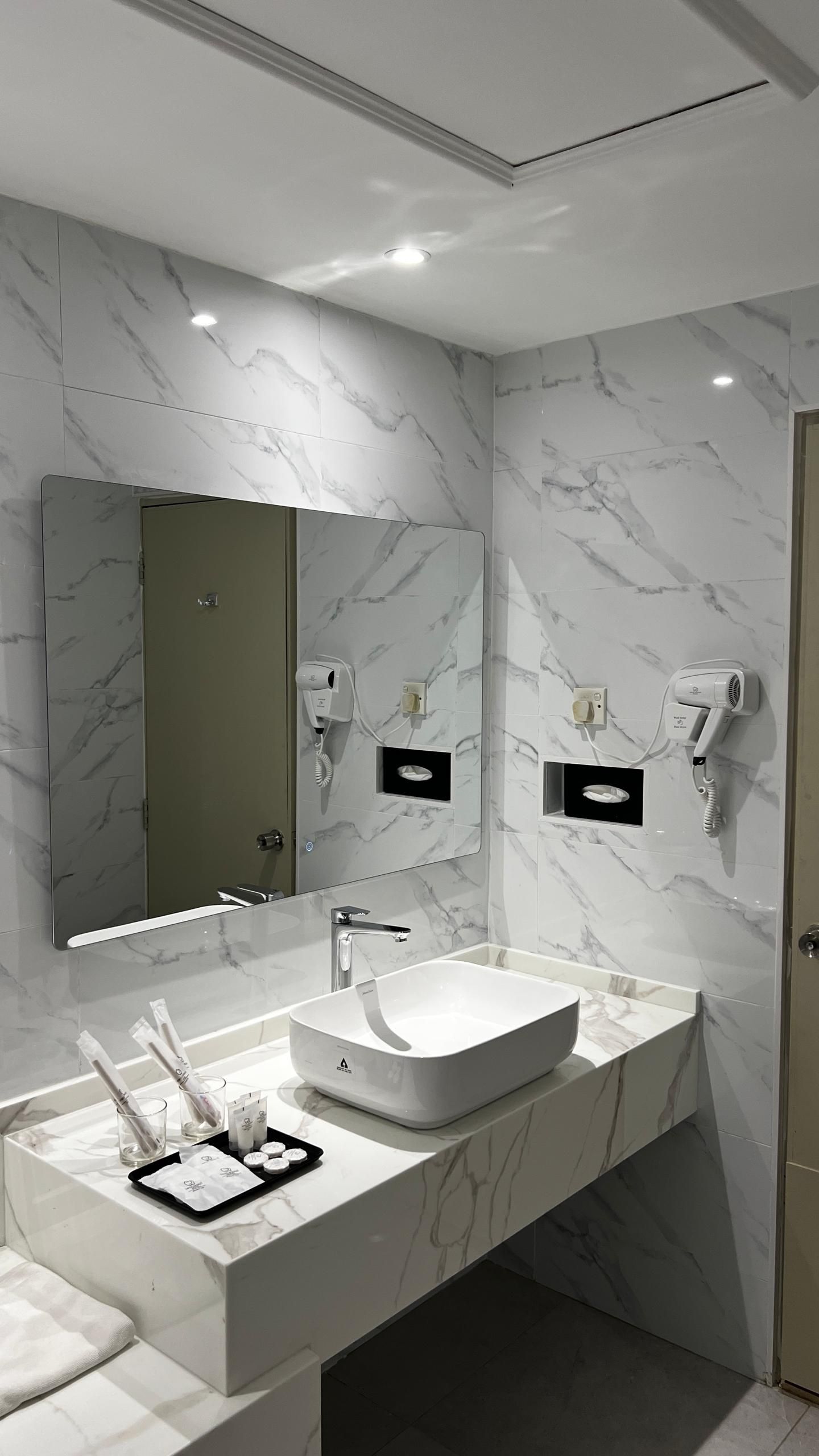 A modern bathroom with a marble backsplash, a large mirror, a white sink, and a towel rack.
