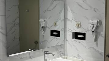 A modern bathroom with a marble backsplash, a large mirror, a white sink, and a towel rack.