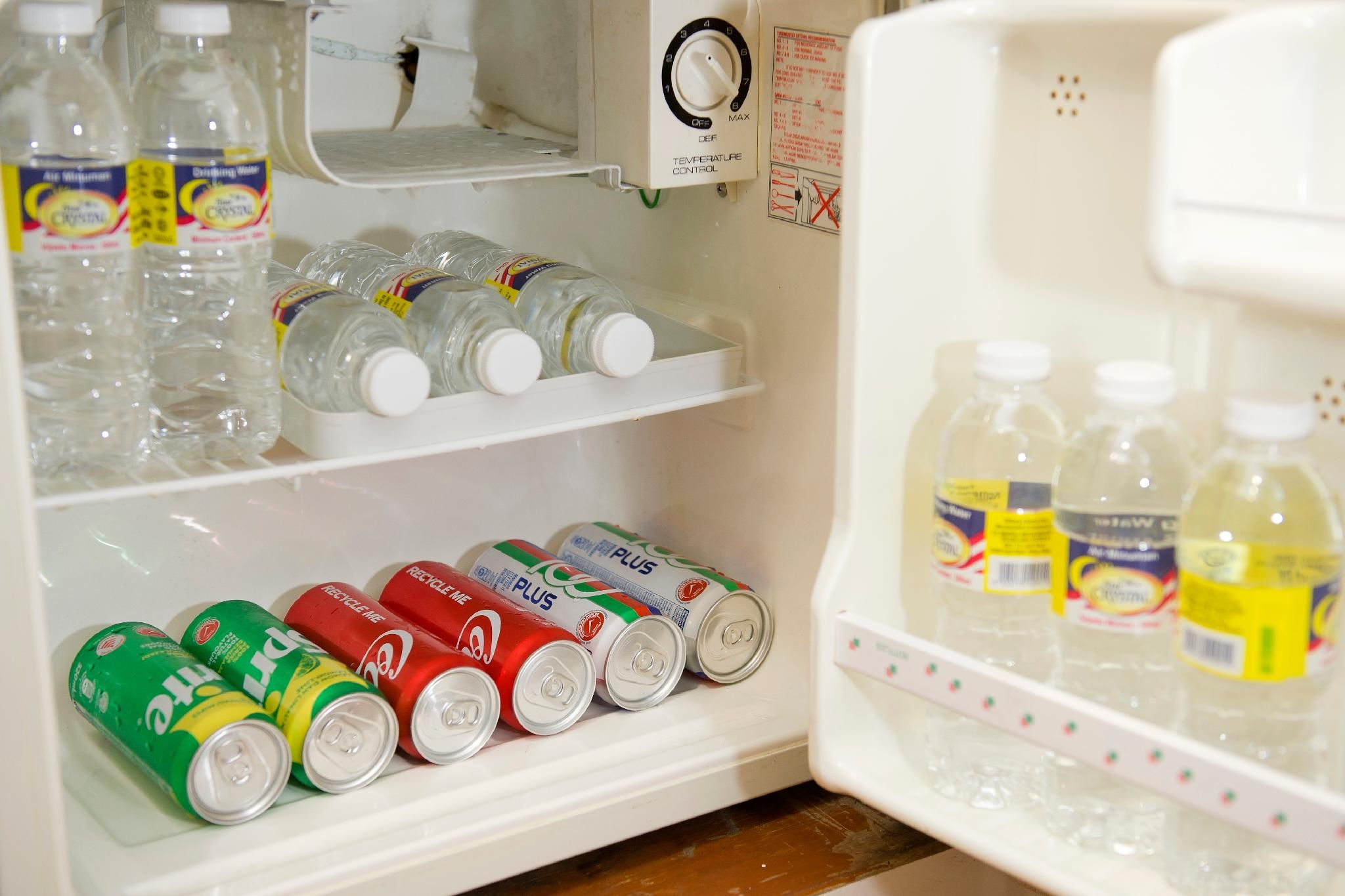 A refrigerator stocked with bottled water, soda cans, and a temperature control dial.