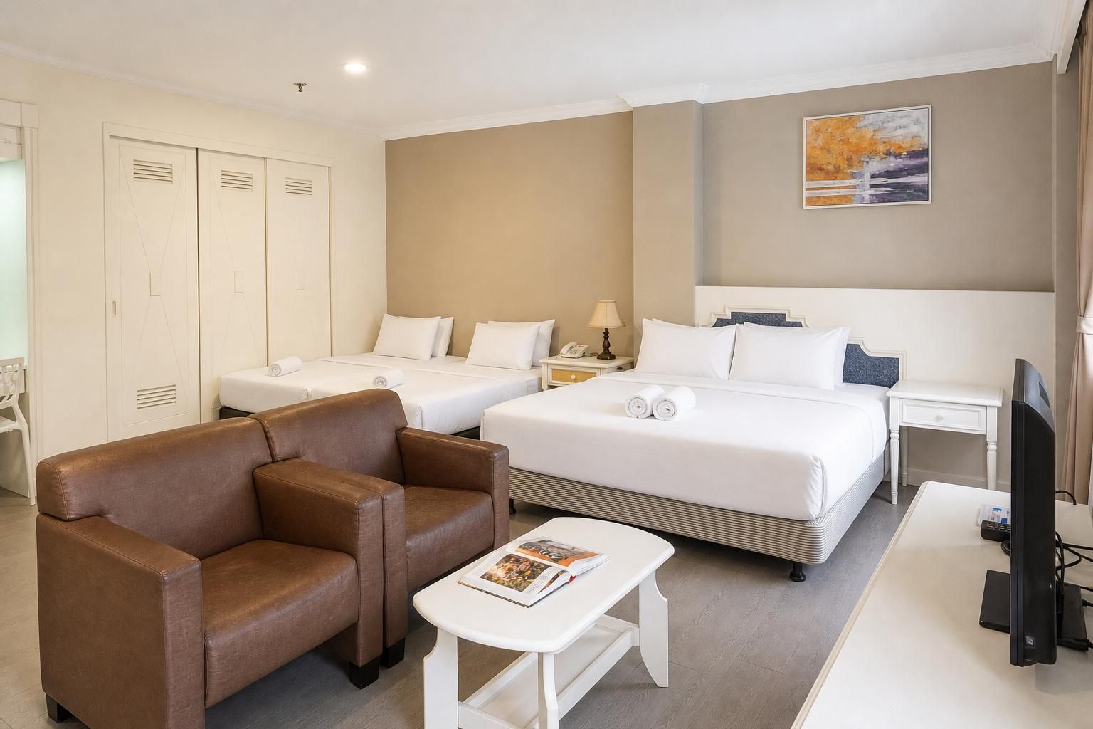 A hotel room with two single beds, a double bed, a brown leather sofa, a white coffee table, and a television.