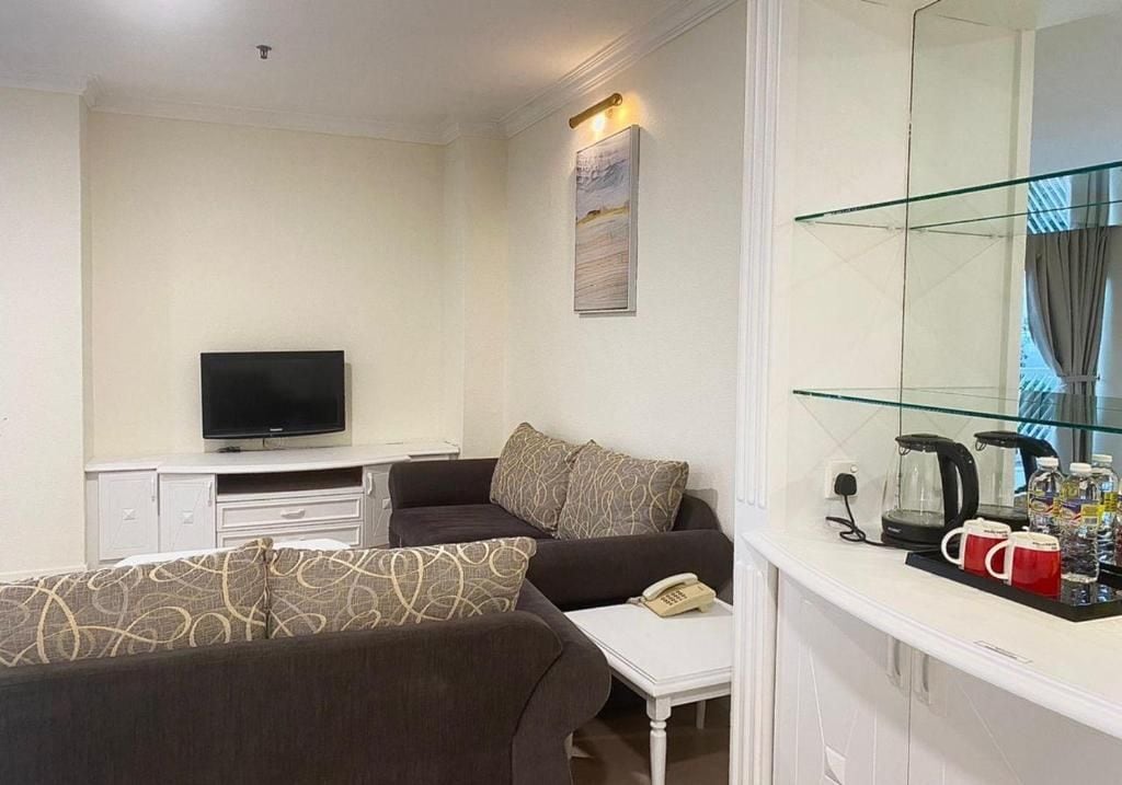 A hotel room with a sofa, a television, a small table with a telephone, and a glass cabinet with items.