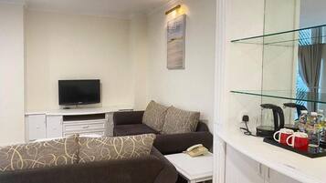 A hotel room with a sofa, a television, a small table with a telephone, and a glass cabinet with items.
