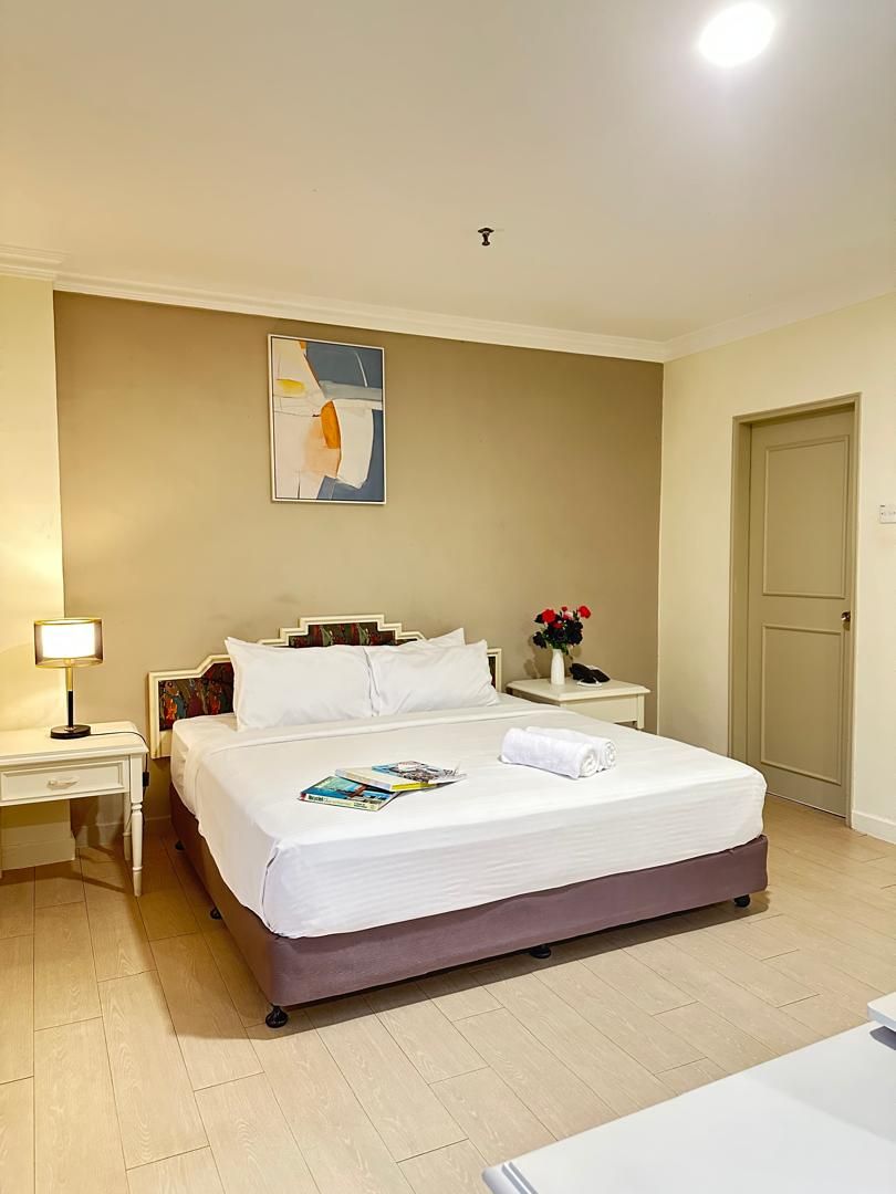 Een hotelkamer met een bed, nachtkastje, lamp, schilderij aan de muur en een deur.