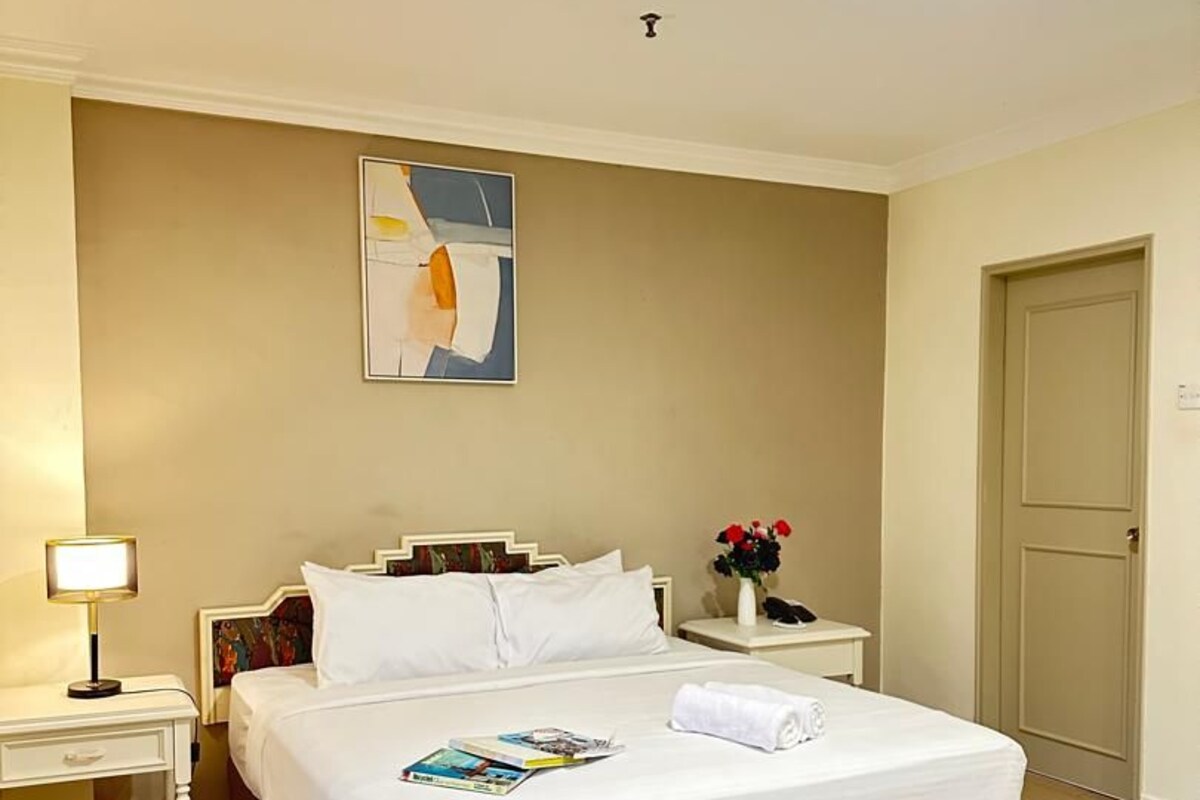 A hotel room with a bed, a nightstand, a lamp, a painting on the wall, and a door.