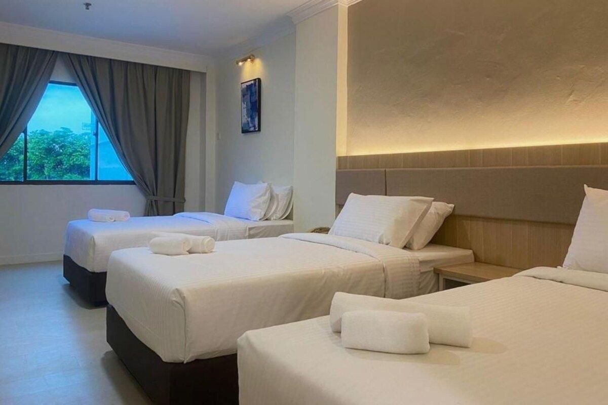 Une chambre d’hôtel avec trois lits, une grande fenêtre avec des rideaux et un luminaire fixé au mur.