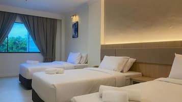 A hotel room with three beds, a large window with curtains, and a wall-mounted light.