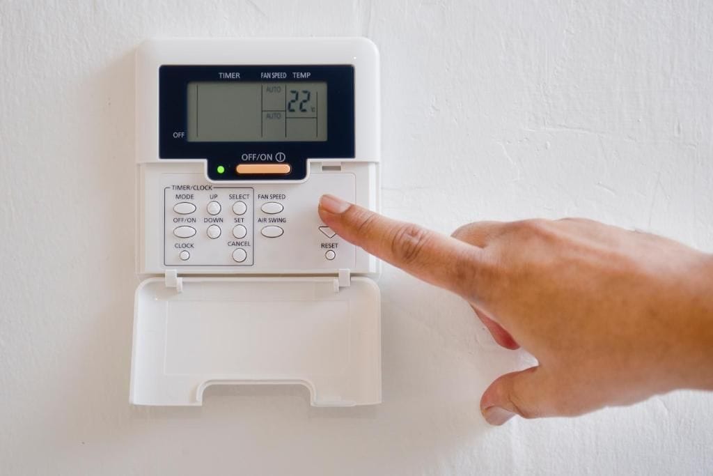 Un termostato con pantalla digital, botones de control y una mano señalando la temperatura ajustada.