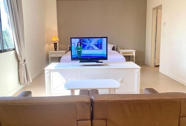 A hotel room with a bed, a television on a stand, a small table, and a bench.