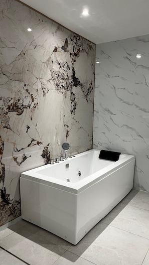 A modern bathroom with a rectangular bathtub, marble walls, and a tiled floor. - Swiss Avenue Hotel (Sungai Petani)