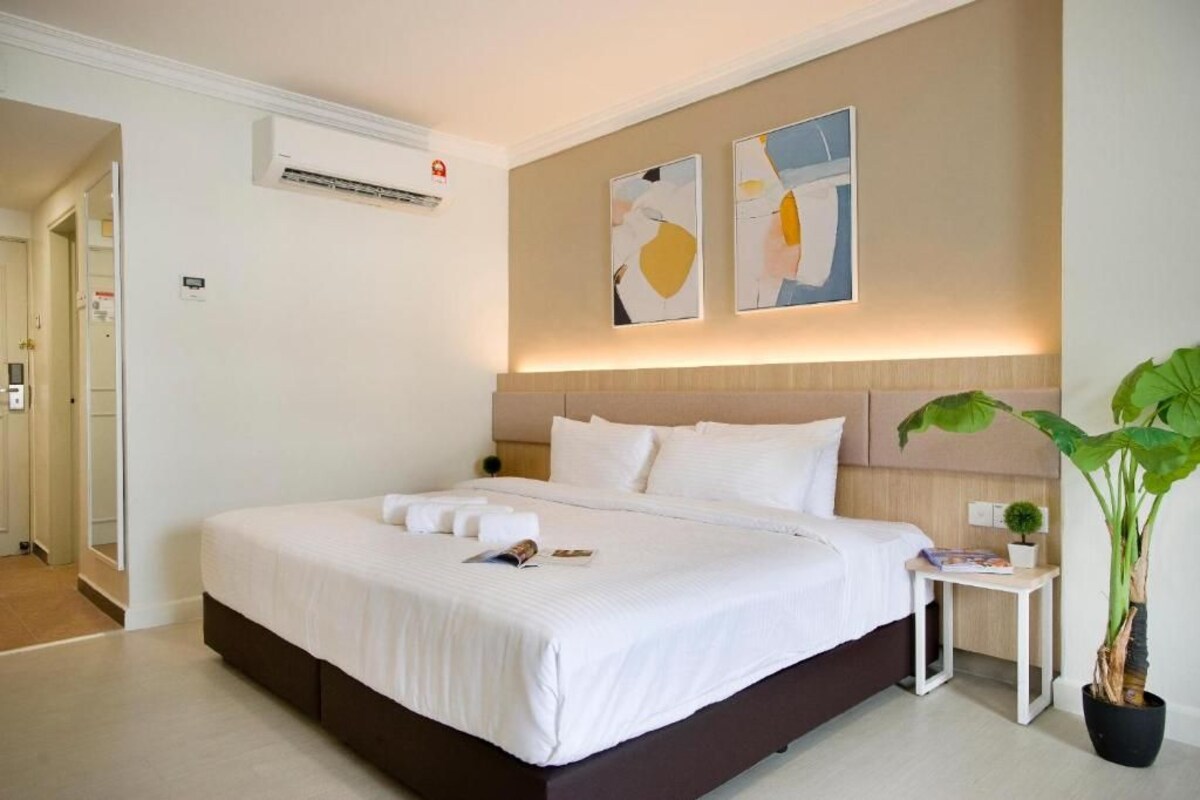Une chambre d’hôtel avec un grand lit, une table de chevet, une plante en pot et des œuvres d’art abstraites accrochées au mur.
