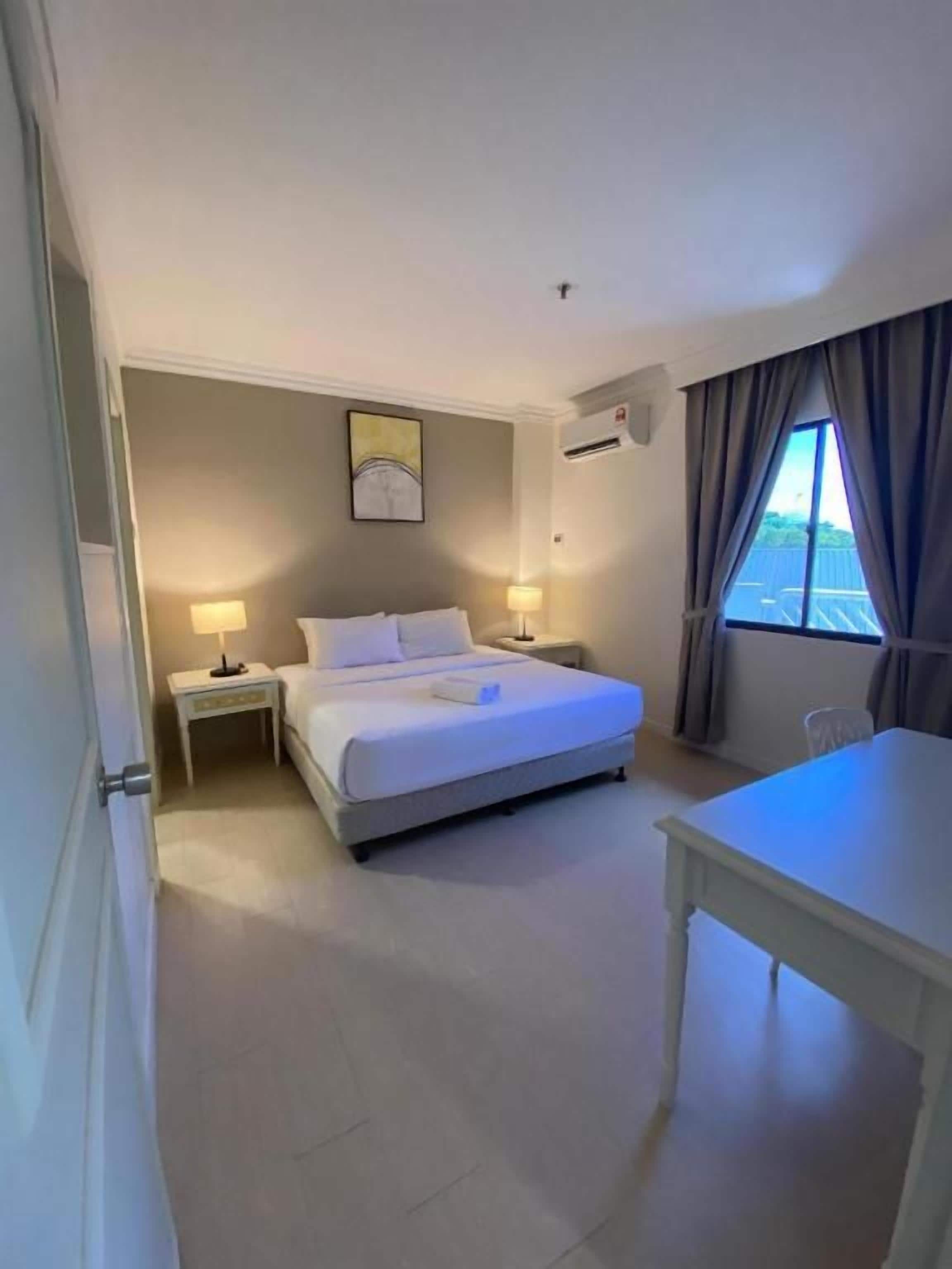 A hotel room with a bed, bedside tables, a desk, and a window with curtains.
