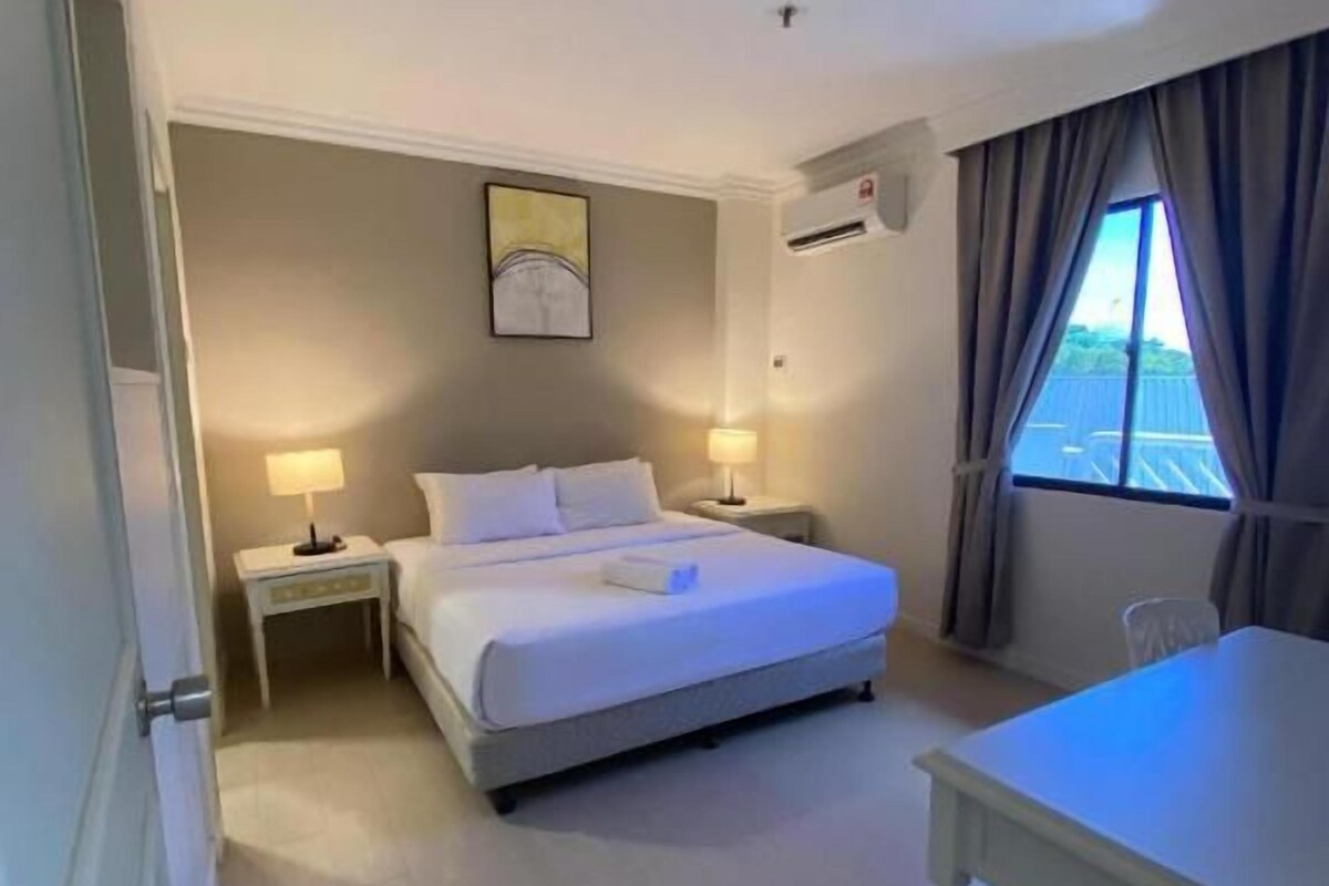 Une chambre d’hôtel avec un lit, des tables de chevet, un bureau et une fenêtre avec des rideaux.