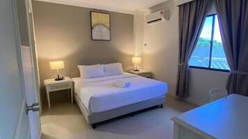 A hotel room with a bed, bedside tables, a desk, and a window with curtains.