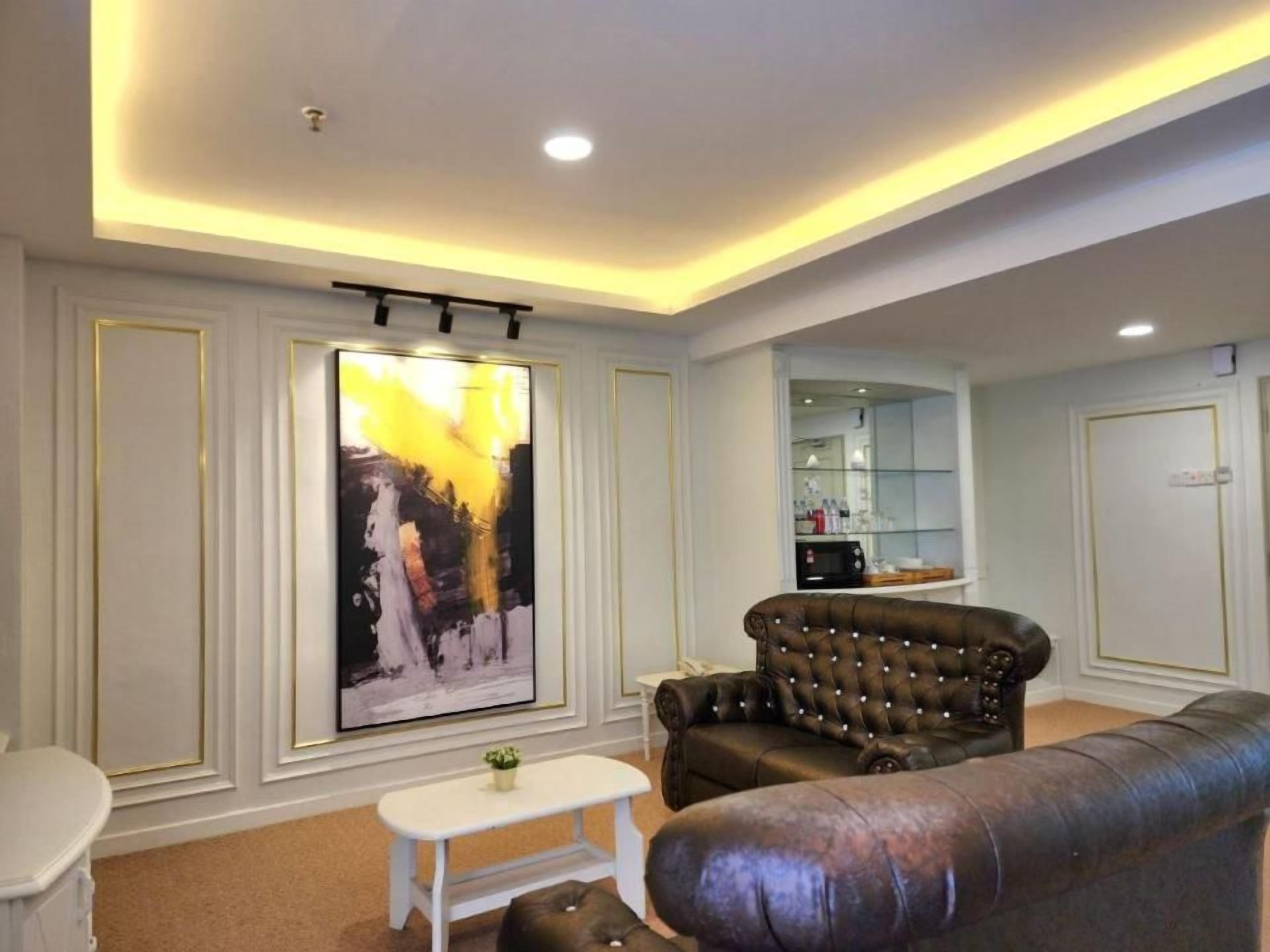 A living room with a large painting, a leather sofa, a white coffee table, and a kitchen area in the background.