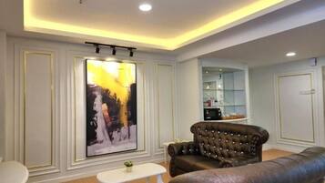 A living room with a large painting, a leather sofa, a white coffee table, and a kitchen area in the background.