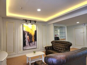 A living room with a large painting, a leather sofa, a white coffee table, and a kitchen area in the background.