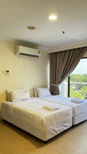 A hotel room with two beds, an air conditioning unit, a window with curtains, and a view of greenery.