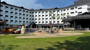 Une cour d’hôtel avec une piscine, des espaces de détente en plein air et un grand bâtiment à plusieurs étages équipé de climatiseurs.