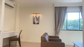 A room with a desk, two chairs, a sofa, a painting on the wall, and a window with curtains.