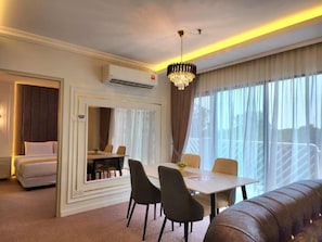 Une chambre d’hôtel avec un lit, un coin repas, un lustre et de grandes fenêtres.