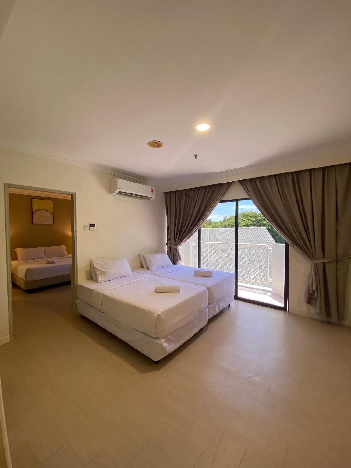 A hotel room with a double bed, a separate bed, an air conditioning unit, and a view of the outside through a large window.