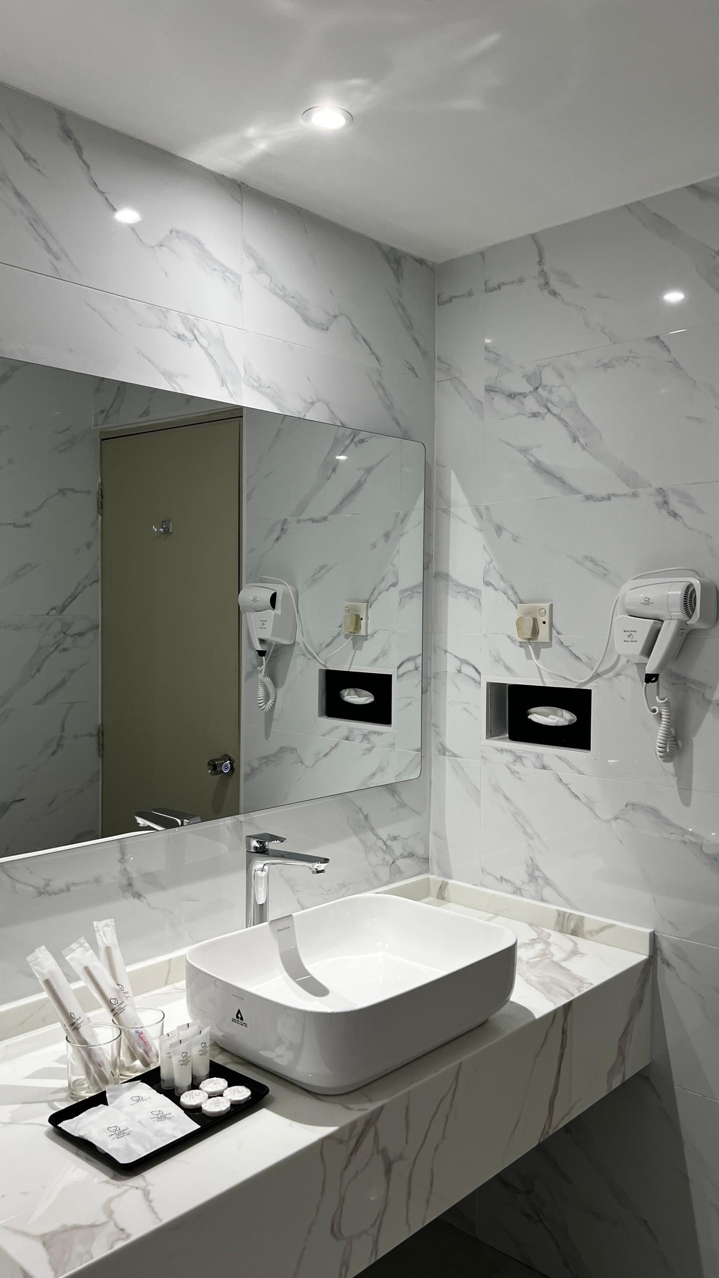A modern bathroom with a large mirror, a white sink, and marble walls.