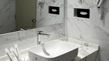 A modern bathroom with a large mirror, a white sink, and marble walls.