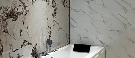 Une salle de bain moderne dotée d’une grande baignoire, de murs en marbre et d’un design minimaliste.
