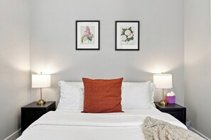 A hotel room with a bed, two bedside tables, two wall-mounted lamps, and two framed botanical illustrations. - Craftsman Bungalow in D'heart of the Arts District (Houston)