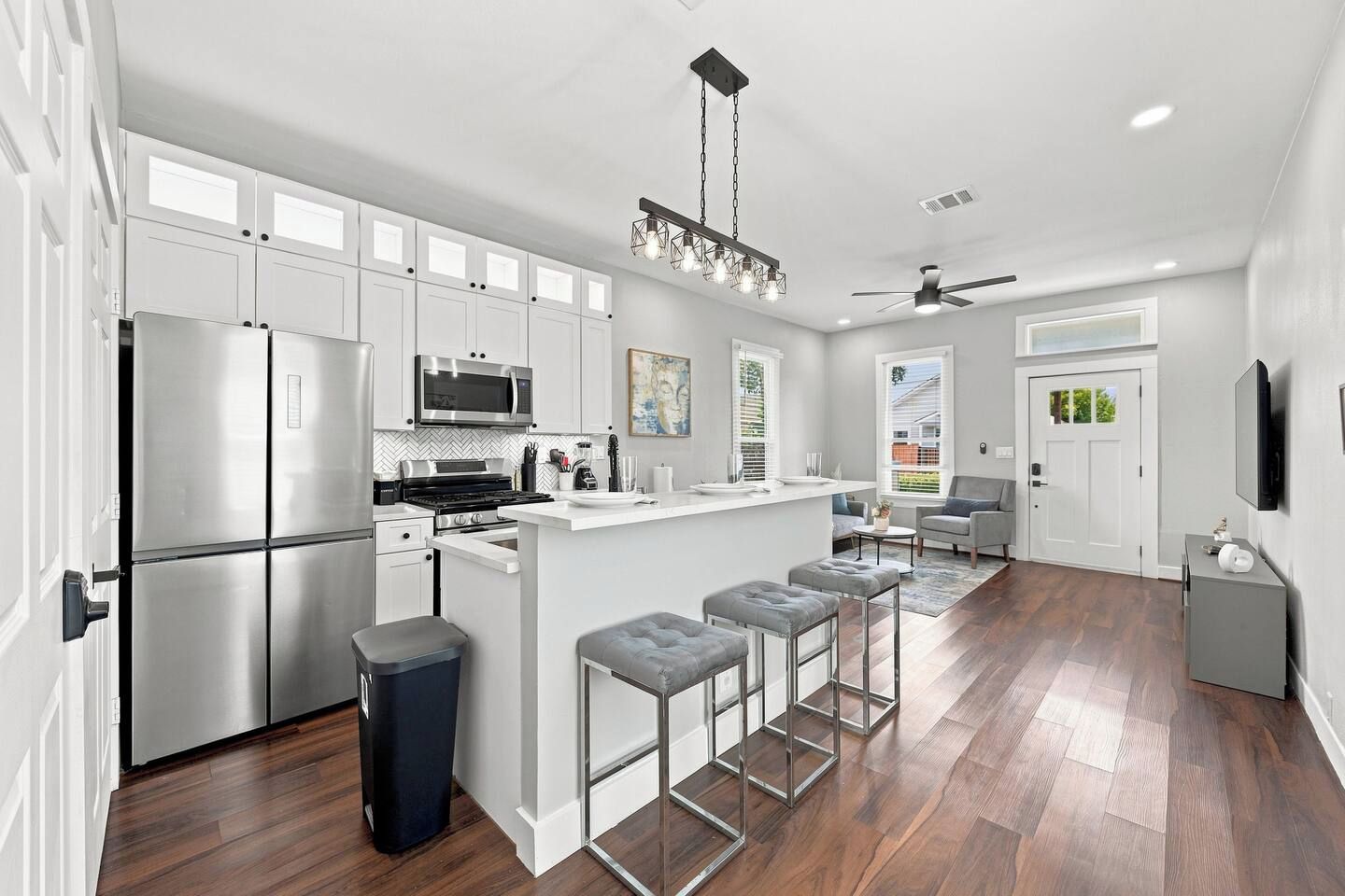 A modern kitchen with stainless steel appliances, a bar area with stools, and a ceiling fan.