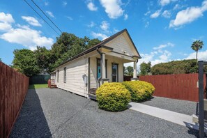 A single-story building with a covered porch, a gravel driveway, and a fenced yard. - Craftsman Bungalow in D'heart of the Arts District (Houston)