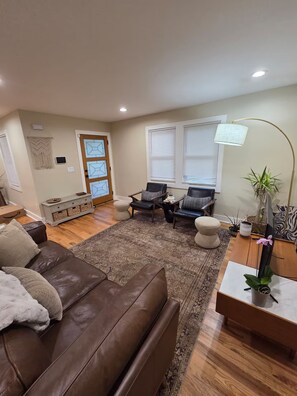 A living room with a brown leather sofa, two armchairs, a coffee table, and a rug. There is a door with geometric glass panels, a macrame wall hanging, and a potted plant. - Home away from home. Cozy. Comfortable. Clean (Atlanta)