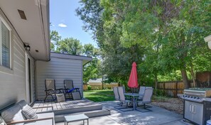 Un patio con mobiliario exterior, una parrilla y una zona cubierta con un paraguas rojo.