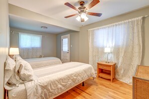 Ein Schlafzimmer mit zwei Betten, einem Deckenventilator, einem Nachttisch mit Lampe und einem Fenster mit gemusterten Vorhängen.