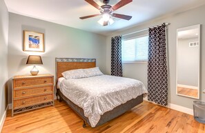 Un dormitorio con cama, ventilador de techo, lámpara de noche, cómoda, ventana con persianas y espejo.