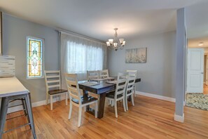 Un comedor con mesa de madera, sillas blancas, una araña y un ventanal de vitral.