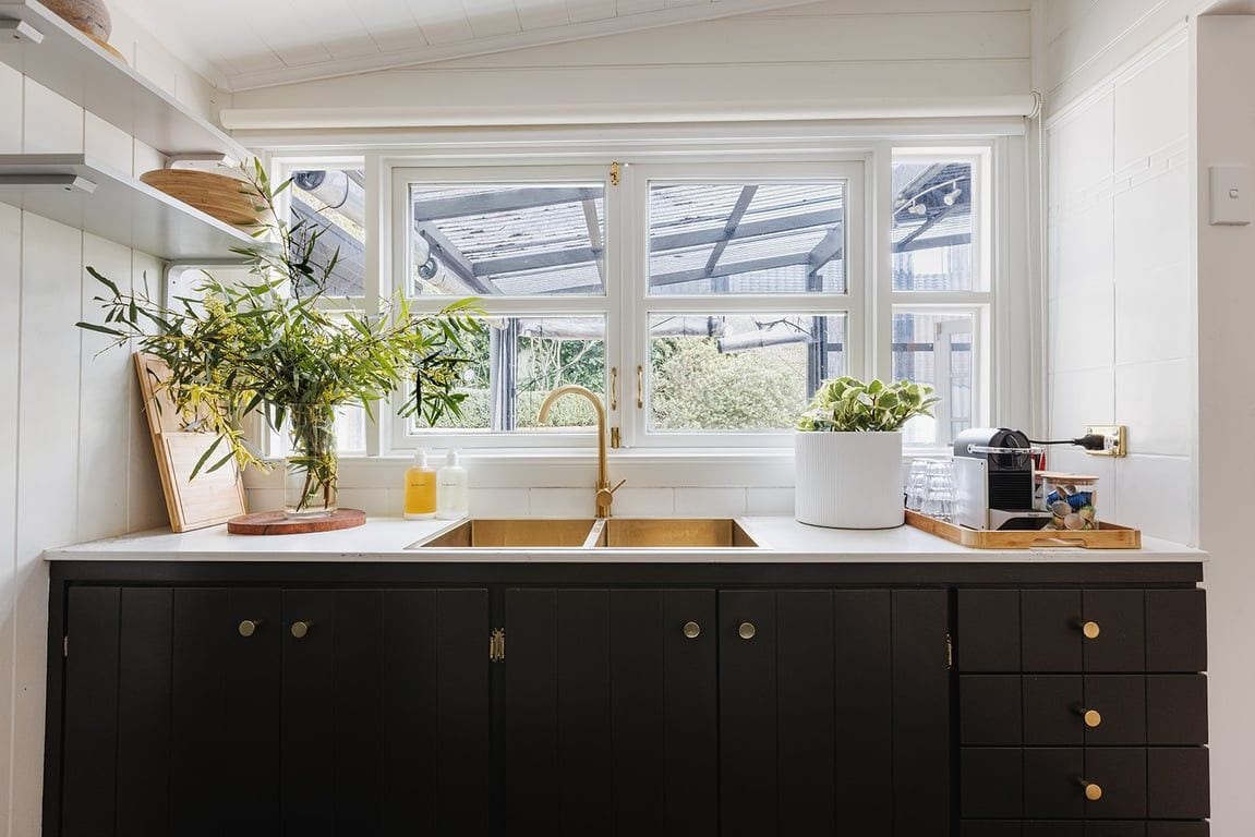 A kitchen with a large window, dark cabinets, and a white countertop.