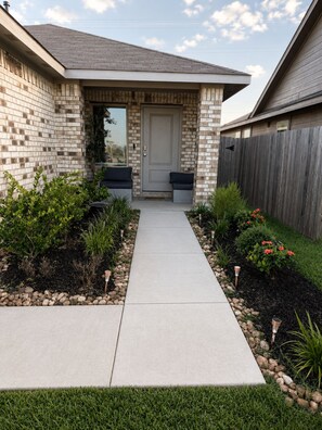 A residential house with a brick exterior, a front porch, and a pathway leading to the door.
