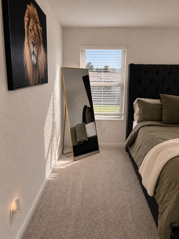 A bedroom with a bed, a large mirror, a painting of a lion, and a window with blinds.